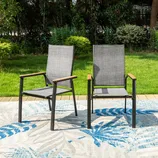 Two modern outdoor chairs with gray mesh fabric and wooden armrests are placed on a patterned rug, set against a green lawn and lush garden background.