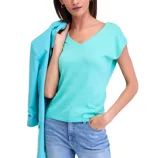 A woman is wearing a light turquoise V-neck sleeveless top paired with light blue jeans. A matching turquoise jacket is draped over her shoulder.