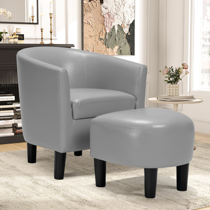 A sleek grey armchair with a matching ottoman featuring black legs, set in a modern living room with a side table, decorative vase, and abstract wall art.