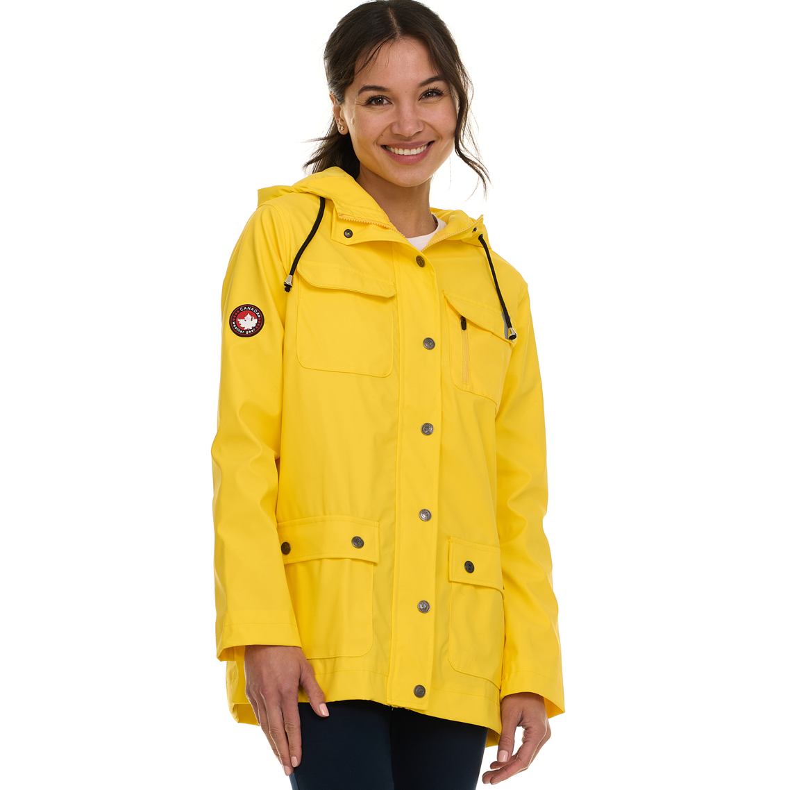 A woman wears a yellow rain jacket with a hood and snap closures. It features two chest pockets, two front flap pockets, and a logo patch on the sleeve.