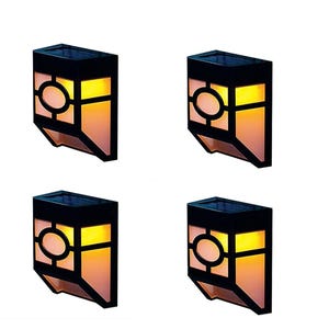 Four LED solar-powered lights designed to attach to a fence display a warm glow through an orange and yellow pane with a circular pattern on the lower section.