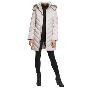 A beige quilted coat with a fur-trimmed hood is worn over a black outfit, paired with black ankle boots.