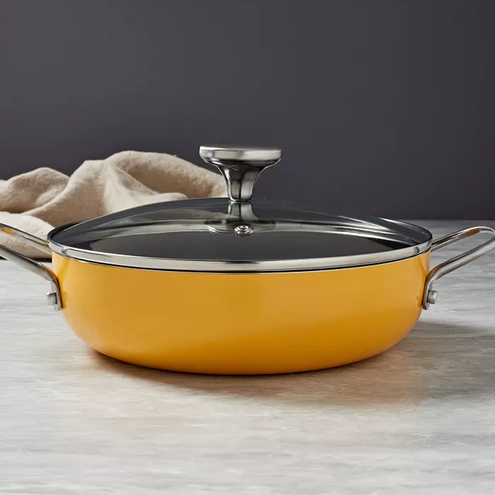 A yellow sauté pan with a glass lid and metal handles on a countertop.