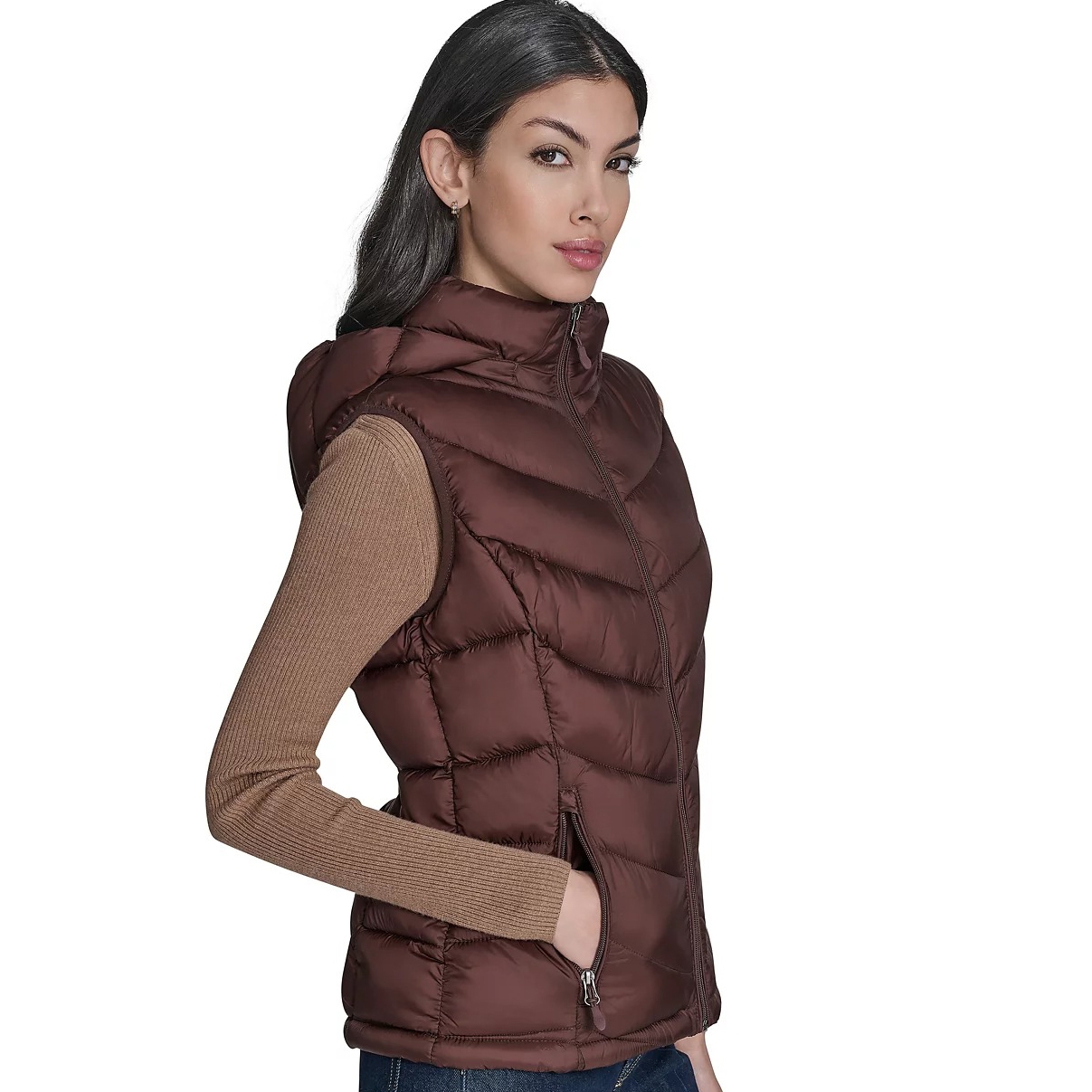 A woman models a brown quilted puffer vest with a hood, over a long-sleeve ribbed tan sweater.