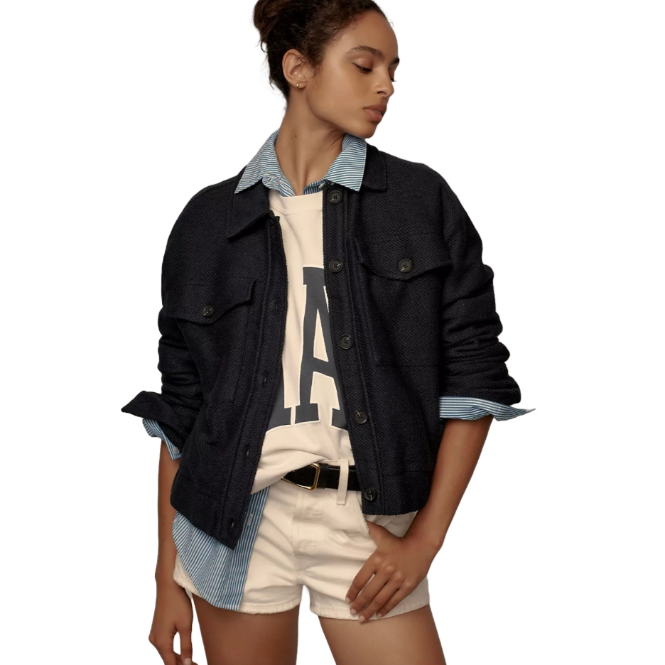 A dark blue bomber jacket with button front and ribbed detailing, worn over a white T-shirt with a letter 'A' and paired with light beige shorts and a striped blue collar shirt.