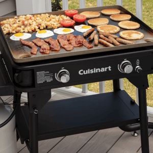 A Cuisinart griddle cooking a variety of breakfast items, including eggs, bacon, pancakes, sausages, tomatoes, and potatoes, on a deck.