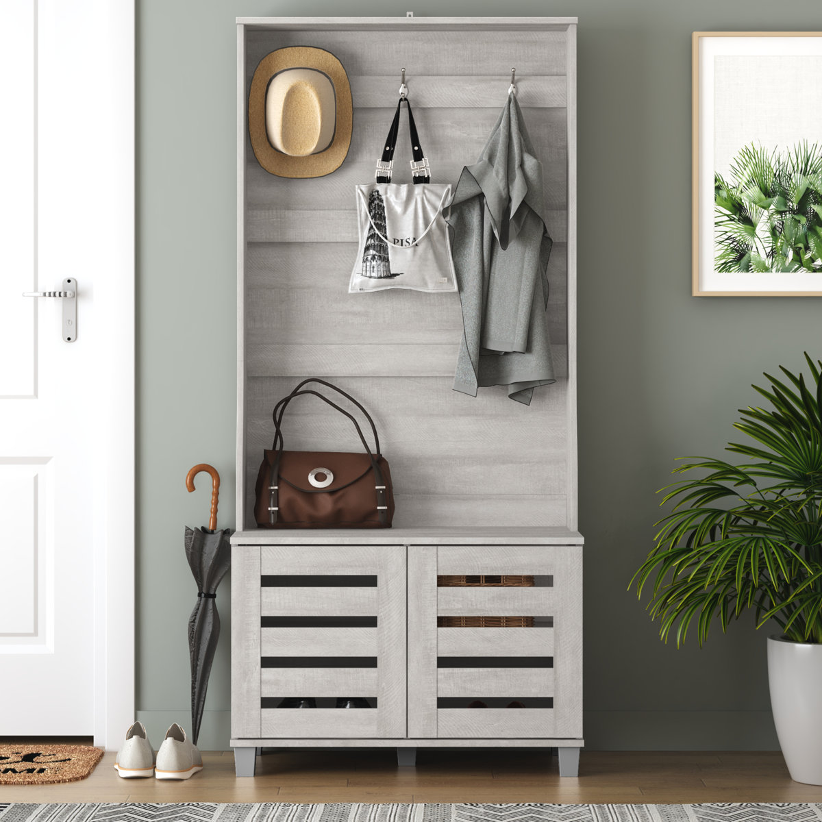 Gray entryway storage unit with hooks for hats, bags, and coats, featuring a lower cabinet for shoes. Accented with a brown bag, umbrella, and nearby plant.