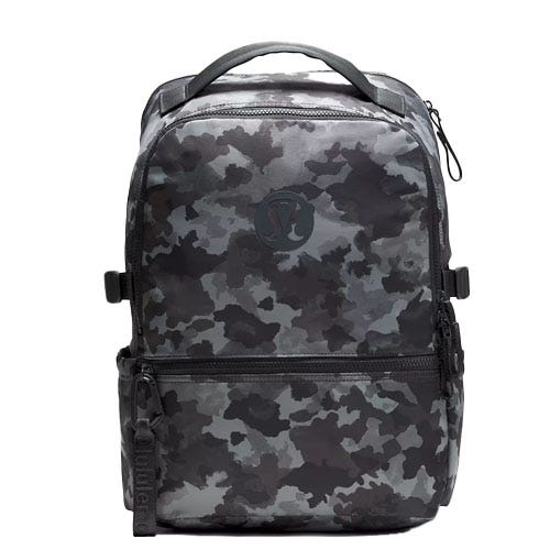 A camouflage-patterned backpack with a top handle, front pocket, and zipper closure, featuring a subtle logo on the front.