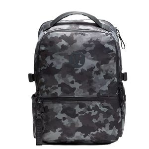 A camouflage-patterned backpack with a top handle, front pocket, and zipper closure, featuring a subtle logo on the front.