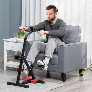 A man is sitting on a gray armchair using a compact stationary exercise bike placed in front of him.