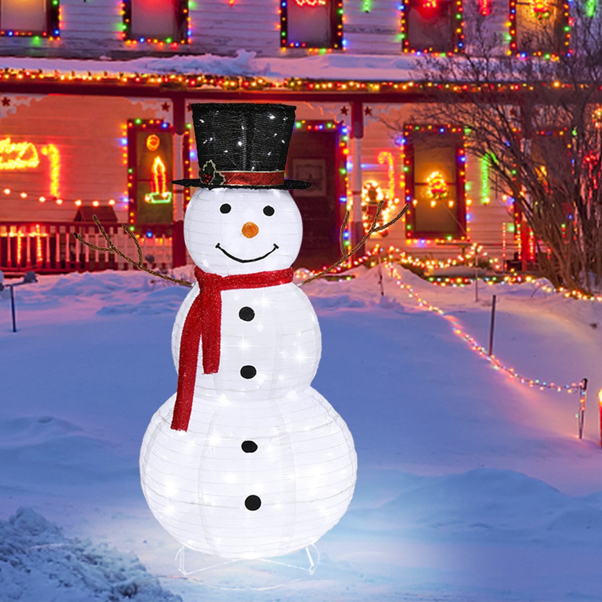 LED snowman decoration with a top hat, red scarf, and stick arms, featured in a snowy yard with a background of a house adorned with colorful Christmas lights.