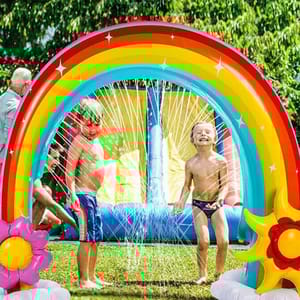 An inflatable rainbow-shaped water sprinkler toy with two children playing underneath.