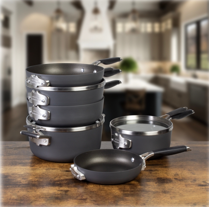 A set of gray non-stick pots and pans with black handles is displayed on a wooden surface, with a blurred kitchen background.