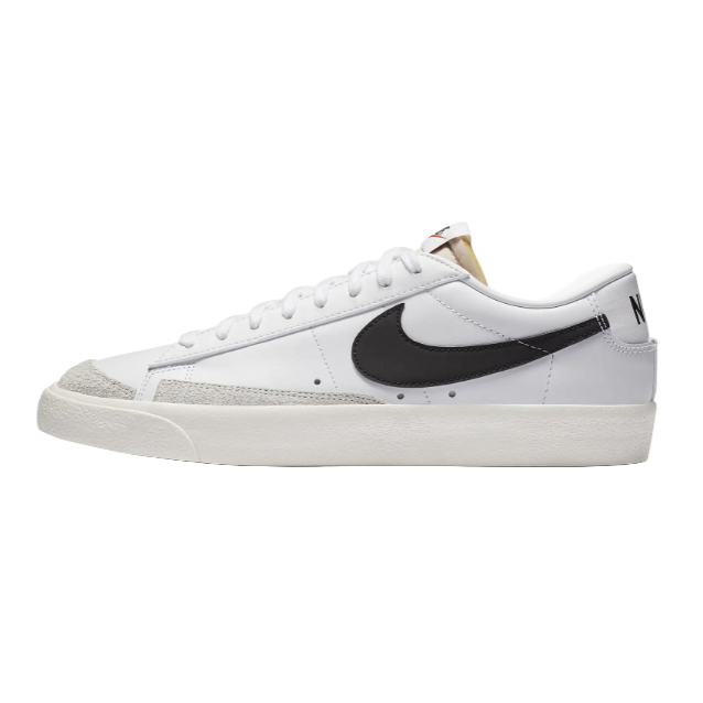 White low-top Nike Blazer Vintage shoes feature a black swoosh, beige suede accents on the toe, and a white rubber sole. The heel displays \“NIKE\“ in black text.