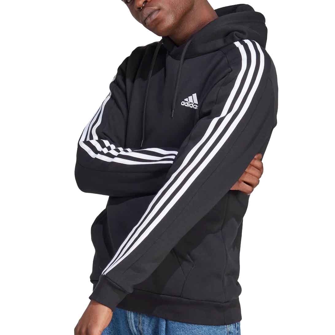 A person wears a black Adidas hoodie featuring white stripes on the sleeves and the Adidas logo on the chest. They pair it with blue jeans.