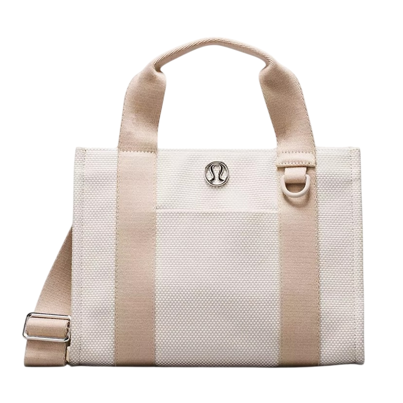 A cream and beige tote bag with dual handles, silver logo emblem, and an adjustable shoulder strap.