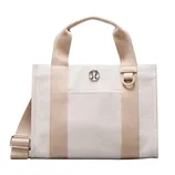 A cream and beige tote bag with dual handles, silver logo emblem, and an adjustable shoulder strap.