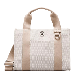 A cream and beige tote bag with dual handles, silver logo emblem, and an adjustable shoulder strap.
