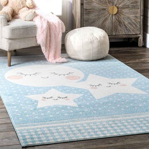Blue and white area rug featuring a smiling moon and stars with closed eyes, set against a polka dot background.