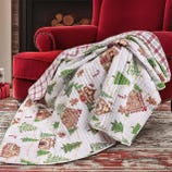A cozy holiday-themed quilt draped over a red armchair features gingerbread houses, Christmas trees, candy canes, and gingerbread figures, providing a festive touch.