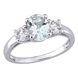 A silver ring featuring an oval-shaped pale green gemstone flanked by two round clear stones in a three-stone setting.