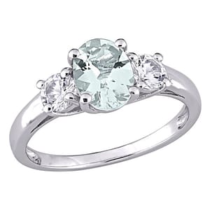A silver ring featuring an oval-shaped pale green gemstone flanked by two round clear stones in a three-stone setting.