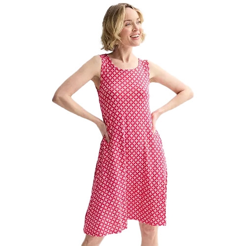 A woman is wearing a sleeveless red and white patterned knee-length dress with a fitted waist and flared skirt, smiling with her hands on her hips.