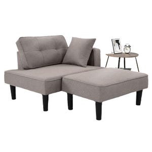 A modular, light gray fabric recliner sofa with a detachable ottoman and black legs, accompanied by a matching pillow. A small round side table with an alarm clock and picture frame is positioned nearby.