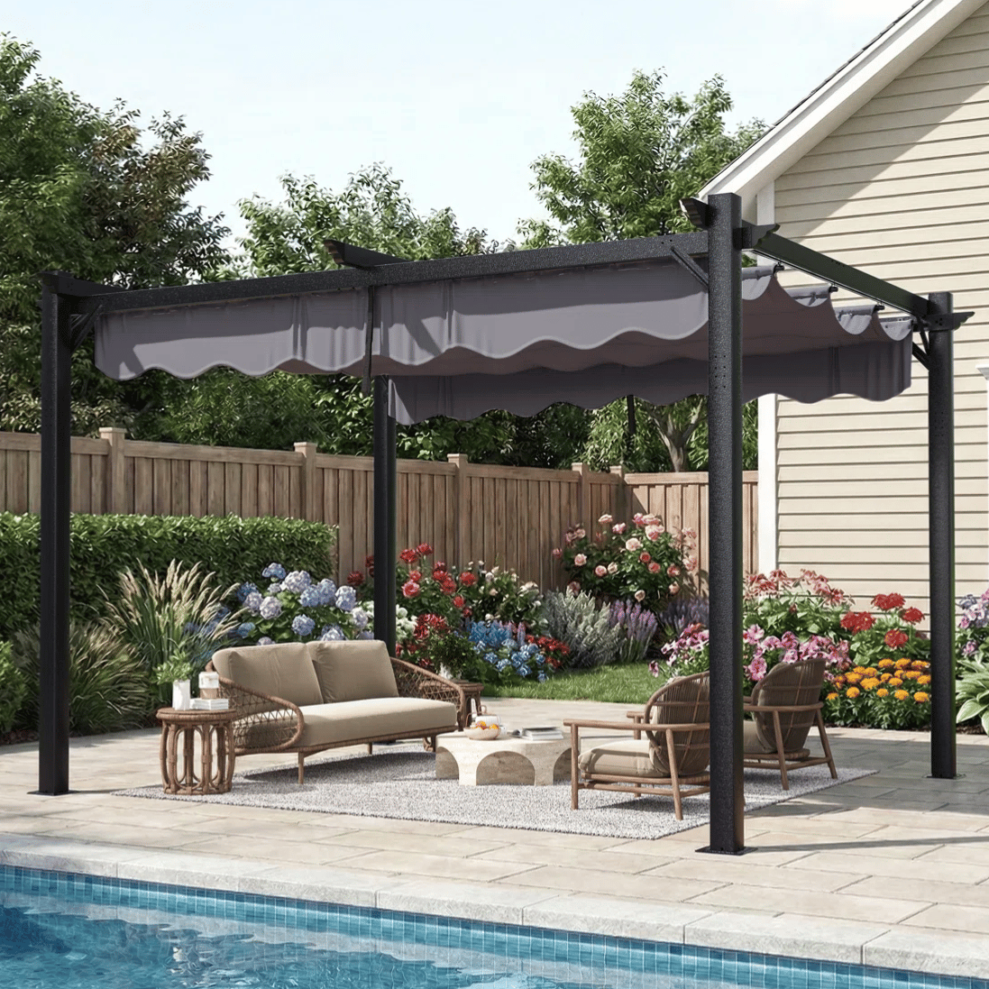 A pergola with a retractable canopy is set up by a pool; it's complemented by outdoor furniture, including a sofa, chairs, a coffee table, and a rug. Lush flower beds and a fence are in the background.