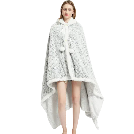 A woman is wearing a white patterned cape with fur trim and pom-pom ties, styled like a cozy cloak or wrap with an elegant drape.
