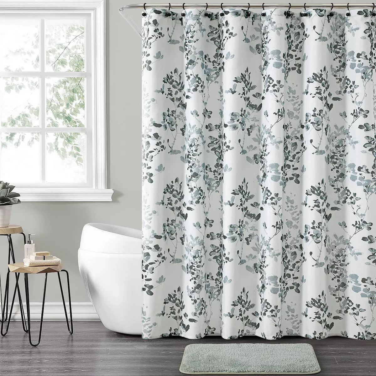 A floral-patterned shower curtain, a freestanding bathtub, and a small rug in front of the tub.