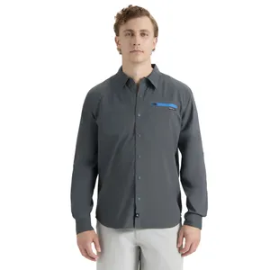 A man is wearing a dark gray button-up shirt with a blue zippered pocket accent on the chest. The shirt has long sleeves and is paired with light gray pants.