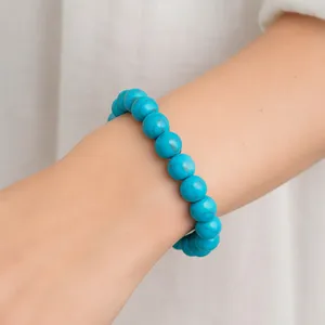 A turquoise beaded bracelet is worn on a person's wrist, featuring round, polished beads.