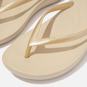 Gold-toned FitFlop iQushion flip-flops featuring a textured strap and cushioned sole with subtle dot patterning for comfort.
