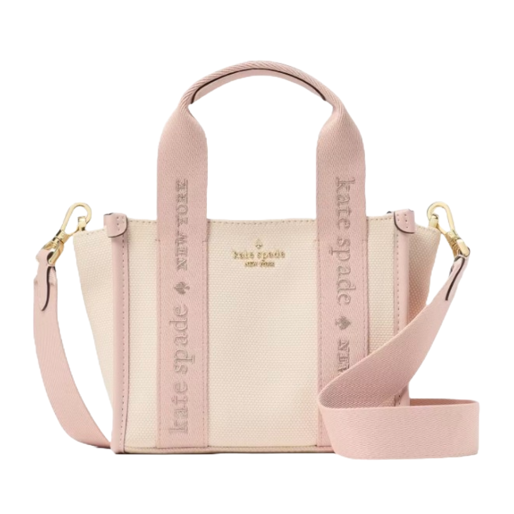 A beige and pink canvas mini tote with dual handles and an adjustable shoulder strap. Gold-tone hardware and \“kate spade new york\“ logo are visible, with the brand name also embossed on the straps.