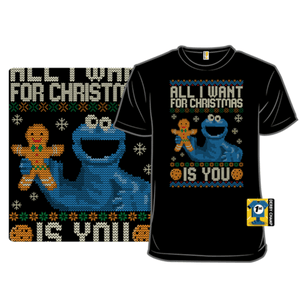 Black T-shirt featuring a festive design with a blue character holding a gingerbread cookie, surrounded by snowflakes, and the text \“All I Want for Christmas is You.\“