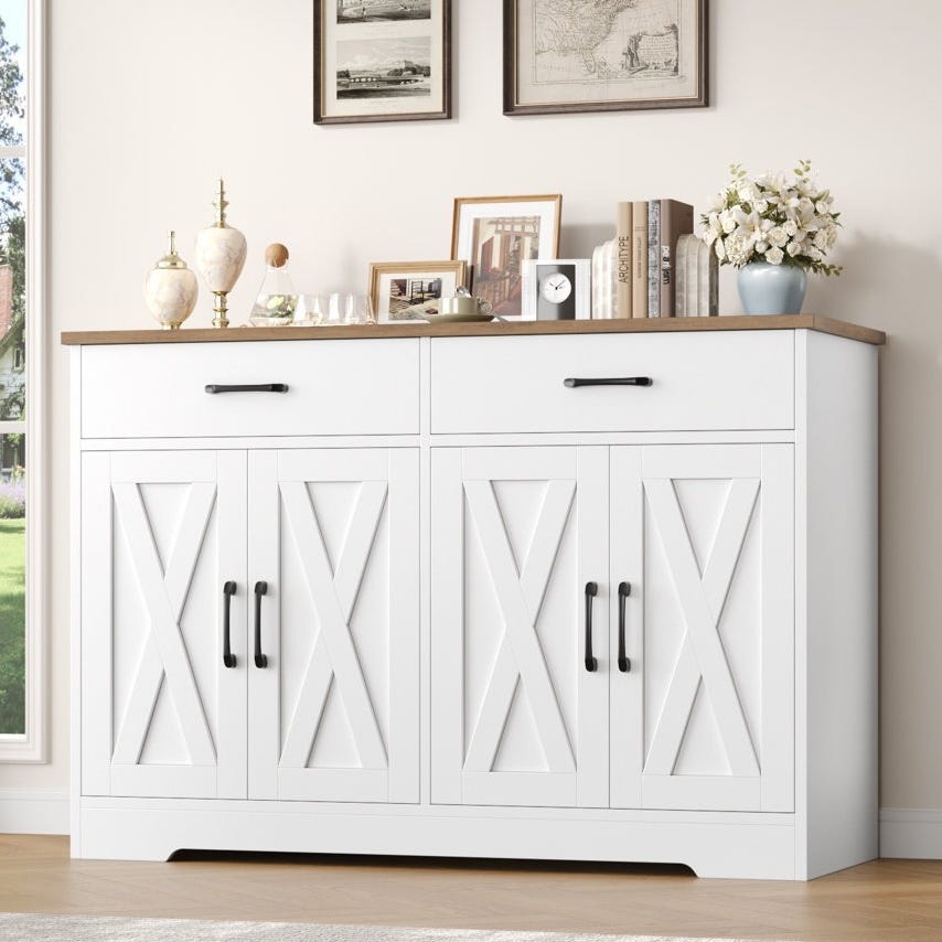 White sideboard cabinet with X-pattern doors, black handles, and a wood countertop. Decor features framed pictures, books, a clock, decorative vases, and a floral arrangement.