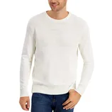 A man wearing a white knitted sweater with textured patterns across the chest and ribbed cuffs and hem, paired with dark blue jeans.