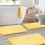 Yellow bath mats and a matching towel adorn a modern bathroom with a freestanding tub, light wood flooring, and a white toilet.
