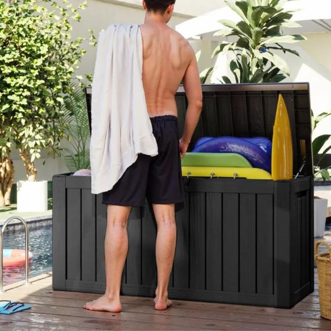 A man stands beside an open, large black storage box containing colorful inflatables and cushions.