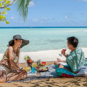 Two people enjoy a beach picnic with food, drinks, and a blanket.