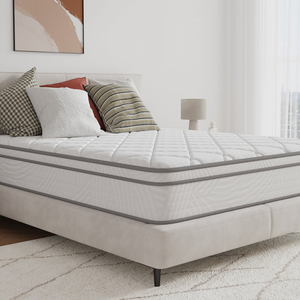 King 12\“ hybrid memory foam mattress in a minimal bedroom setting, featuring a stylish quilted surface with layered cushions, neutral-tone geometric bed frame, assorted pillows, a bedside lamp, and abstract wall art.