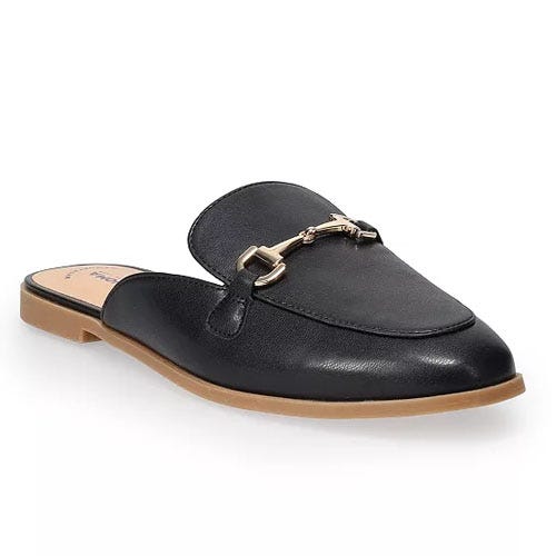 A black slip-on mule shoe with a gold-toned metal bit detail on the upper and a flat, tan sole.