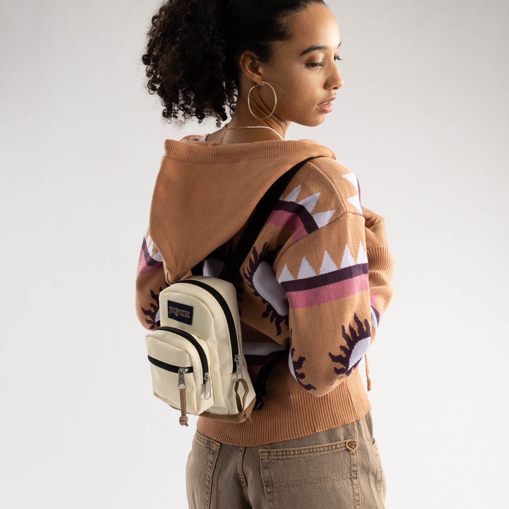 A woman wearing a patterned sweater and hoop earrings, carrying a cream-colored backpack.