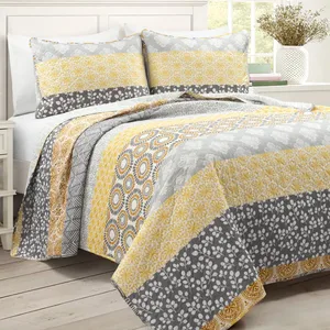 A bed is adorned with a quilt set featuring a combination of yellow, gray, and white floral and geometric patterns, accompanied by matching pillow shams.