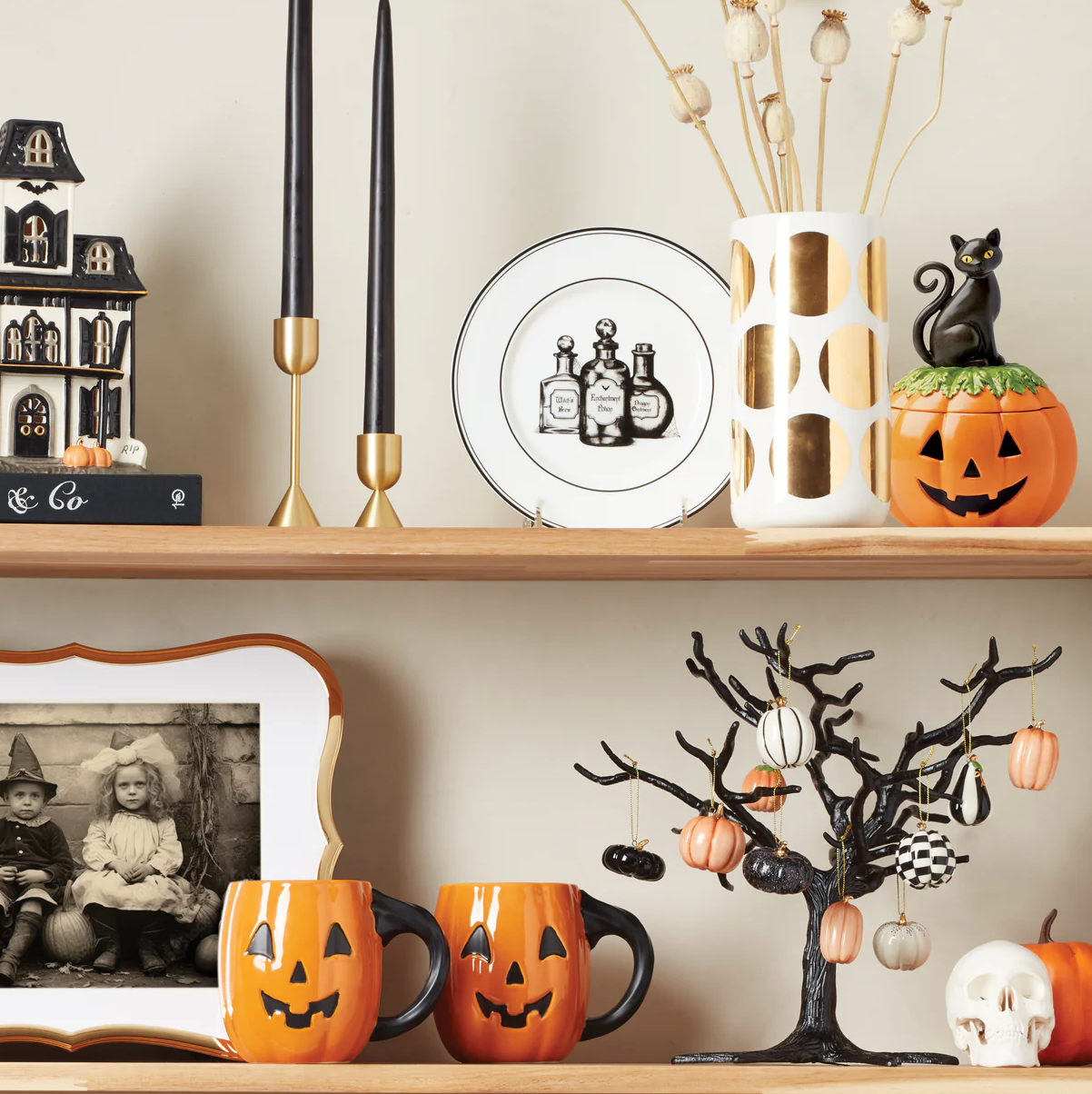Halloween-themed decorations include a haunted house, black candles, a plate with potion bottles, pumpkin mugs, a tree with mini pumpkins, and a black cat on a jack-o'-lantern. A skull and a vintage photo complement the setup.