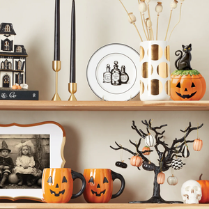Halloween-themed decorations include a haunted house, black candles, a plate with potion bottles, pumpkin mugs, a tree with mini pumpkins, and a black cat on a jack-o'-lantern. A skull and a vintage photo complement the setup.