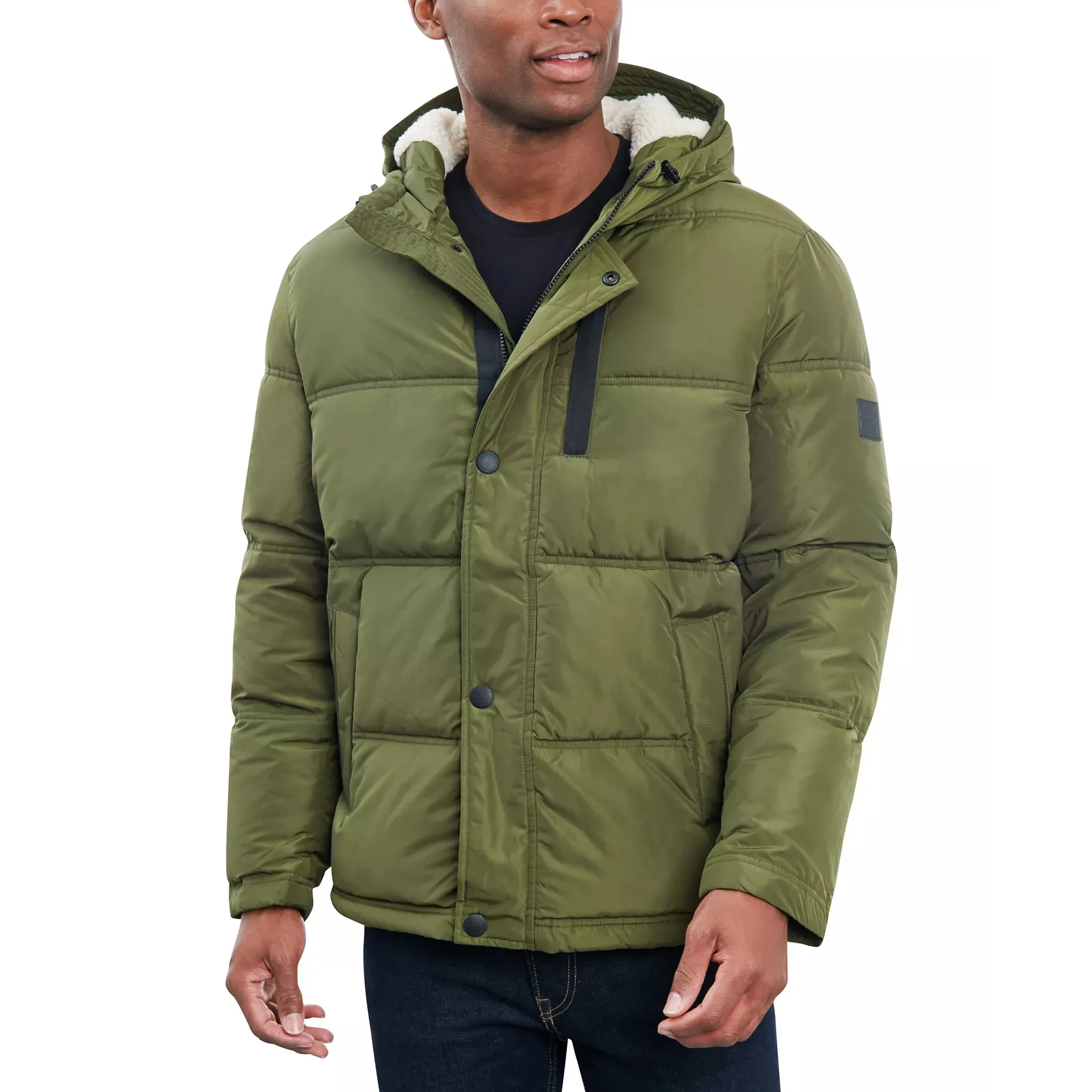 A man wearing an olive green puffer jacket with a hood, black buttons, and a sherpa lining, paired with dark jeans.