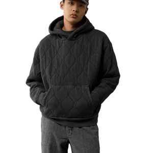 A dark, heavyweight quilted hoodie featuring a textured pattern, kangaroo pocket, and drawstring hood, paired with gray trousers and a cap.