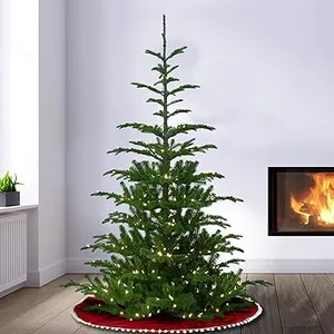 A sparse artificial Christmas tree with minimal branches and warm white lights, placed on a red tree skirt near a lit fireplace.